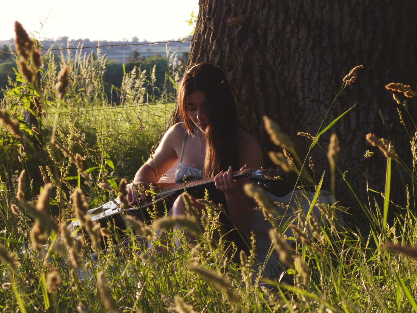 Emmy Bloom playing acoustic guitar in a field